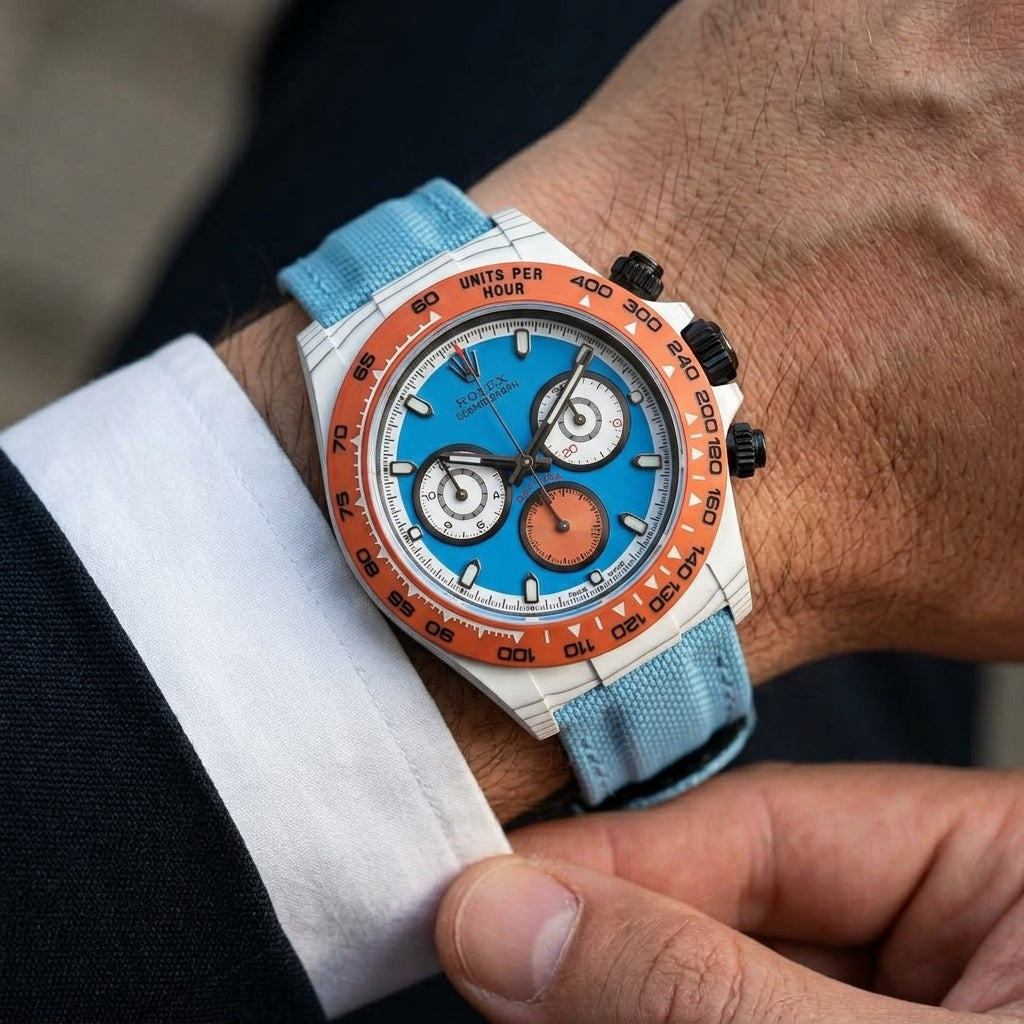 White forged carbon chronograph with an orange bezel and a sky-blue dial on the wrist as a shirt cuff is fastened