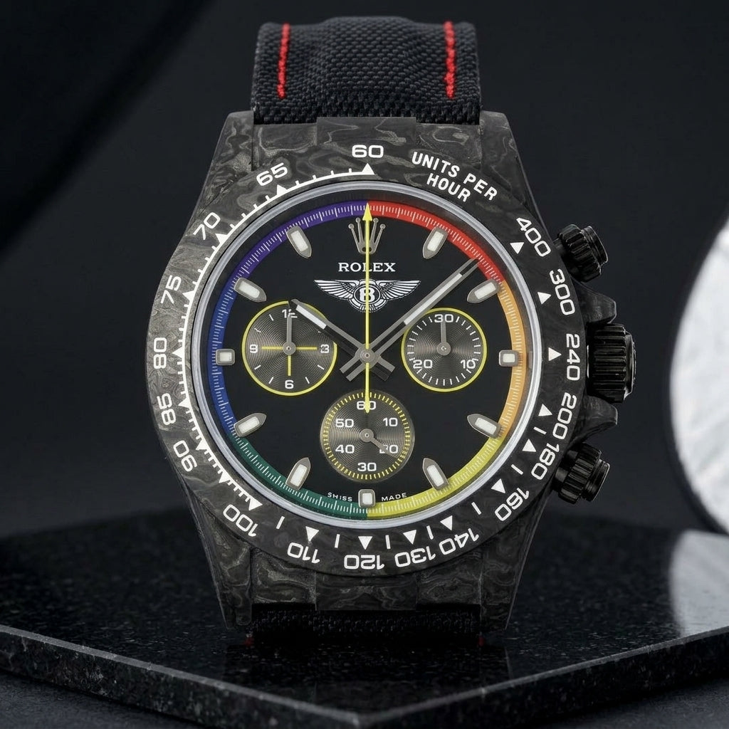 Rainbow-ring forged carbon chronograph on a black strap stitched in red, worn on the wrist below a navy suit cuff
