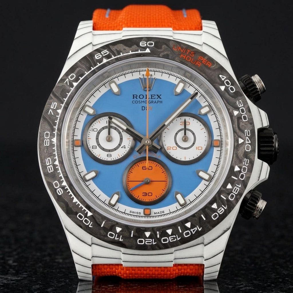 White carbon chronograph with a sky-blue dial on its orange canvas strap, worn on the wrist below a dark suit cuff