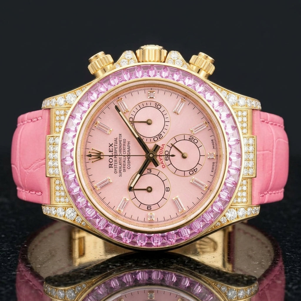Gold chronograph with a pink dial and a pink stone bezel on a pink alligator strap, worn on the wrist below a navy suit cuff