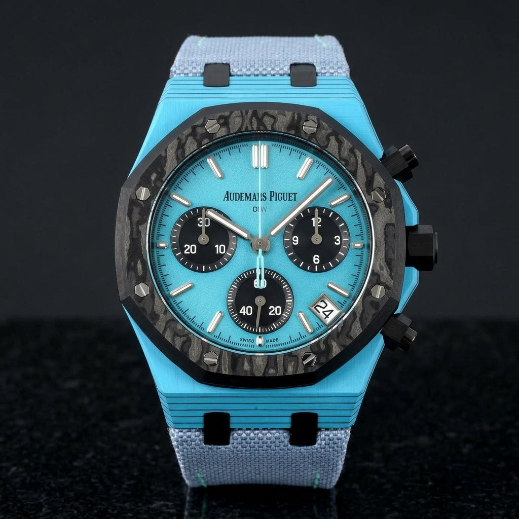 Octagonal chronograph with a sky-blue case on its light-blue canvas strap, worn on the wrist below a dark suit cuff