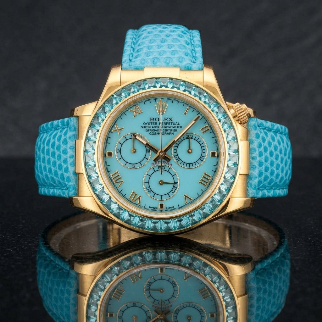 Gold-tone chronograph with a turquoise dial and an aqua-blue stone bezel on a turquoise lizard-grain strap, worn on the wrist below a navy suit cuff