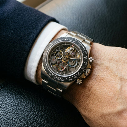 Steel skeleton chronograph with a carbon bezel on its steel bracelet, worn on the wrist below a dark suit cuff