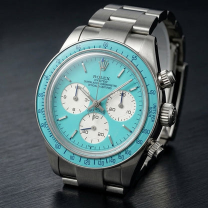 Steel chronograph at a three-quarter angle, the screw-down crown and pushers beside the turquoise bezel