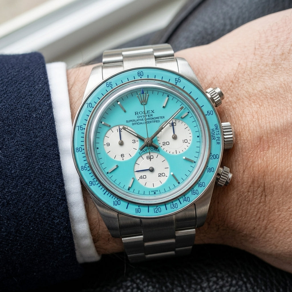 Steel chronograph with a turquoise dial and bezel on the wrist below a dark suit cuff