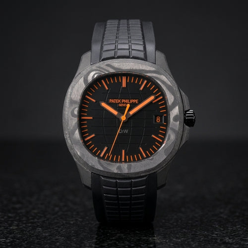 Black forged-carbon grid-dial watch with orange batons and a black rubber strap, upright on polished black granite