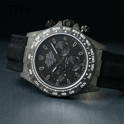 All-black forged-carbon chronograph at a three-quarter angle, white bezel numerals catching the light