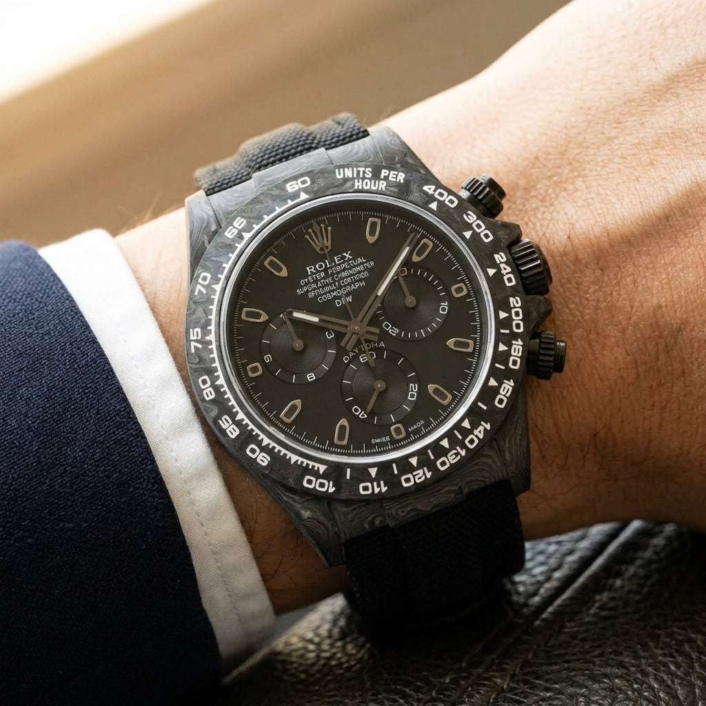 All-black forged-carbon chronograph on a black woven strap, worn under a cuff