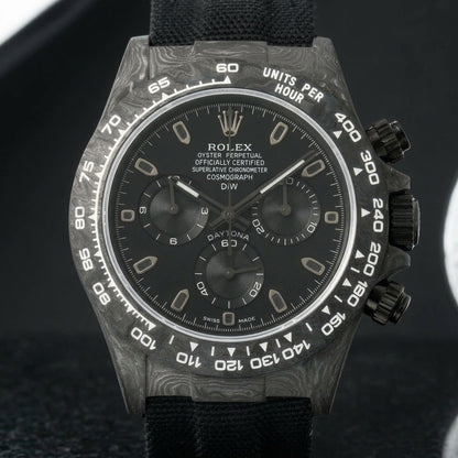 All-black forged-carbon chronograph on a black woven strap, worn under a cuff