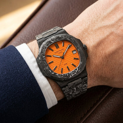 Orange-dial forged carbon sports watch on its black and silver-white carbon bracelet, worn on the wrist below a navy suit cuff