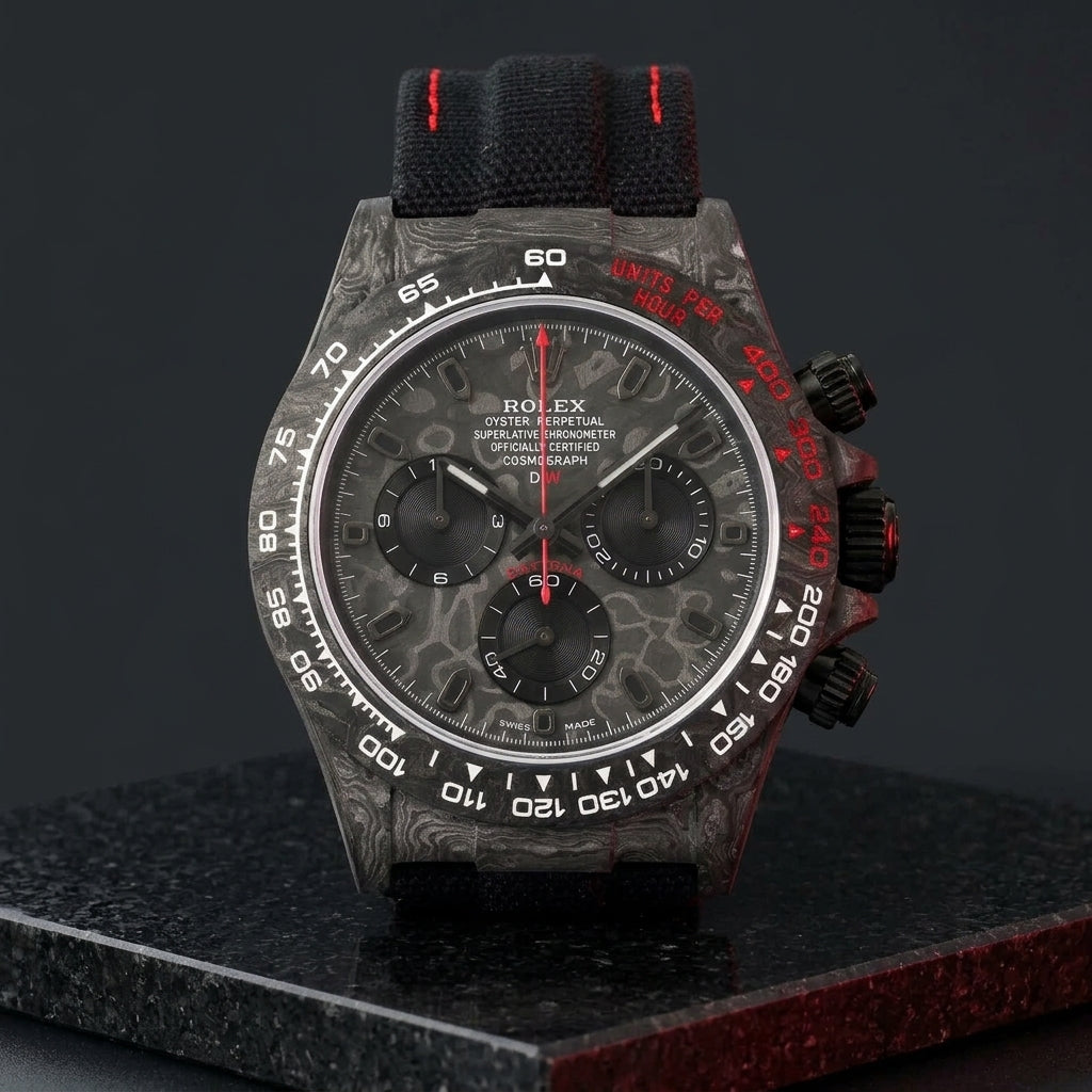Forged-carbon chronograph on a black woven strap with red stitching, worn under a cuff