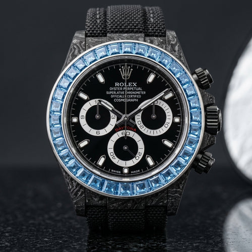 Black forged-carbon chronograph with a sky-blue stone bezel and a black dial, upright on polished black granite