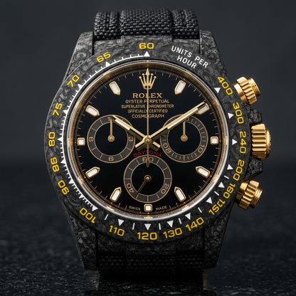 Black carbon chronograph with a black dial and yellow scale on its black woven strap, worn on the wrist below a suit cuff