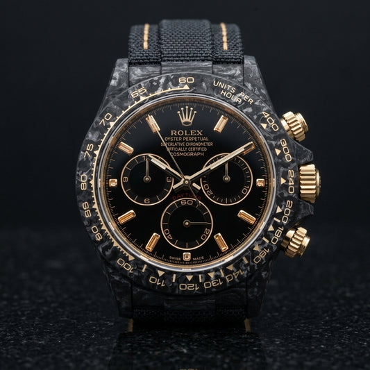 Black forged carbon chronograph with champagne baguette stone markers on a black dial and a pale gold tachymeter scale, upright on polished black granite