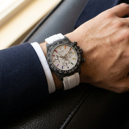Carbon chronograph with a white pavé dial on its white woven strap, worn on the wrist below a navy suit cuff and white shirt