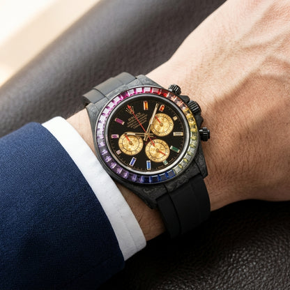 Rainbow bezel carbon chronograph on a black rubber strap worn under a suit cuff