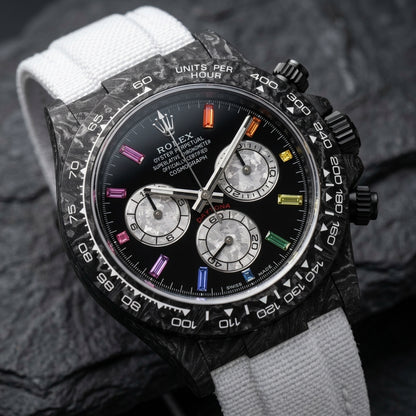 Black forged carbon chronograph at a three-quarter angle on dark slate, the white tachymeter scale on its marbled carbon bezel
