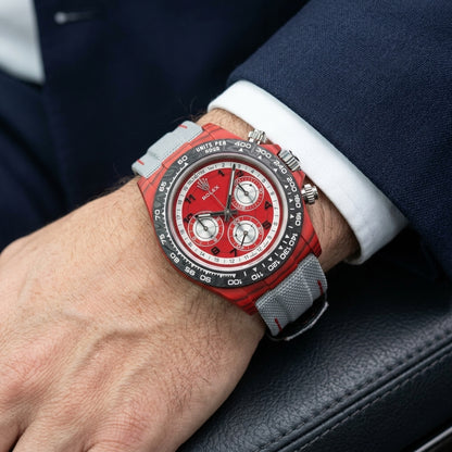 Red carbon chronograph on its light-grey canvas strap with red stitching, worn on the wrist below a navy suit cuff