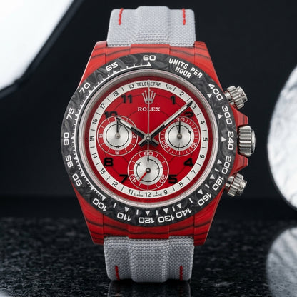 Red carbon chronograph on its light-grey canvas strap with red stitching, worn on the wrist below a navy suit cuff