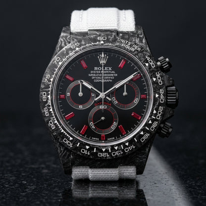 Black forged carbon chronograph with red baguette stone markers on a black dial and a white tachymeter scale, upright on polished black granite
