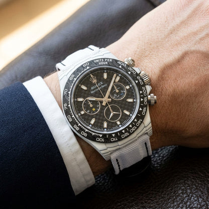 White carbon chronograph on its white woven canvas strap, worn on the wrist below a navy suit cuff