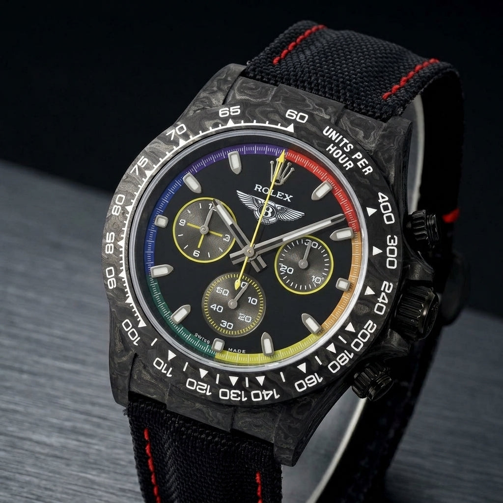 Black forged carbon chronograph at a three-quarter angle on dark slate, its rainbow minute track catching the light