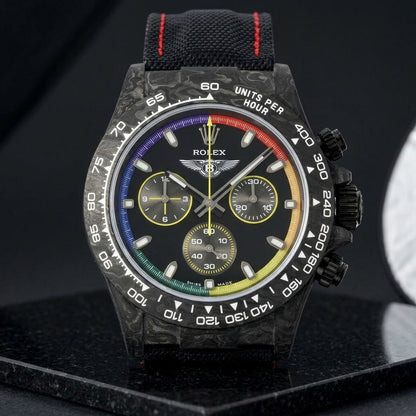 Rainbow-ring forged carbon chronograph on a black strap stitched in red, worn on the wrist below a navy suit cuff