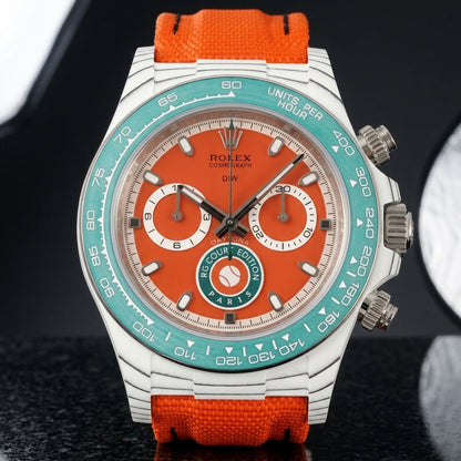 White carbon chronograph with a clay-red dial, a green tennis badge and a teal tachymeter bezel, upright on polished black granite