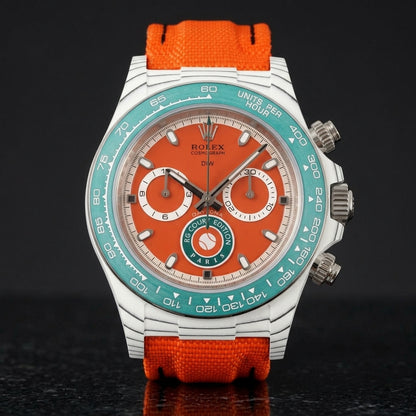 White carbon chronograph with a clay-red dial on its orange canvas strap, worn on the wrist below a dark suit cuff