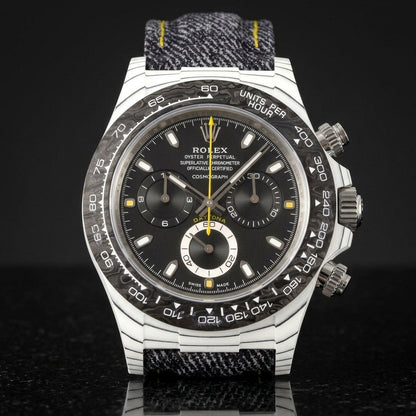 White carbon chronograph with a black forged-carbon bezel, a black dial and a yellow chronograph hand, upright on polished black granite