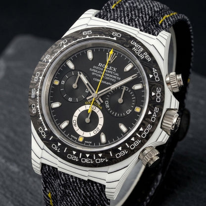 White carbon chronograph at a three-quarter angle on dark slate, its black-lined flank beside the steel crown and pushers