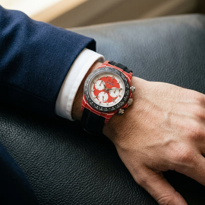 Red carbon chronograph with a red-and-white dial on its black canvas strap with red stitching, worn on the wrist below a dark suit cuff