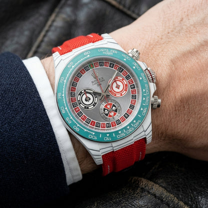White carbon chronograph with a roulette-wheel dial on its red canvas strap, worn on the wrist below a dark suit cuff