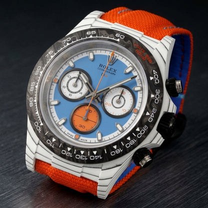 White carbon chronograph at a three-quarter angle on dark slate, the black crown and steel-capped pushers beside the forged-carbon bezel