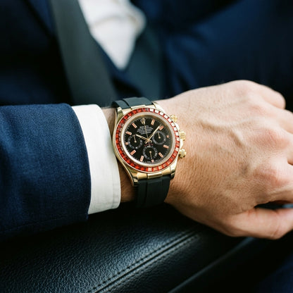 Gold-tone chronograph with a red stone bezel on its black rubber strap, worn on the wrist below a dark suit cuff