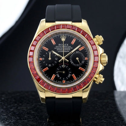 Gold-tone chronograph with a red stone bezel on its black rubber strap, worn on the wrist below a dark suit cuff