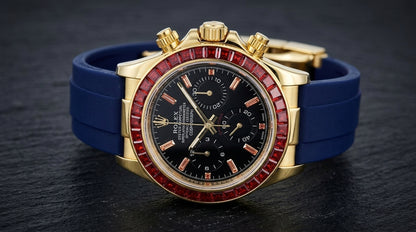 Gold chronograph at a three-quarter angle on dark slate, the fluted crown and pushers beside the ring of red baguette-cut stones