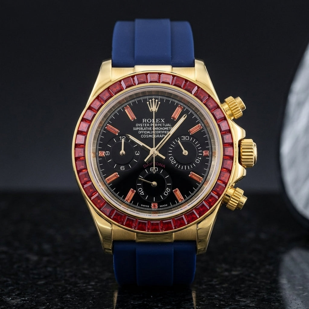 Gold chronograph with a red stone bezel on its navy blue rubber strap, worn on the wrist below a dark suit cuff