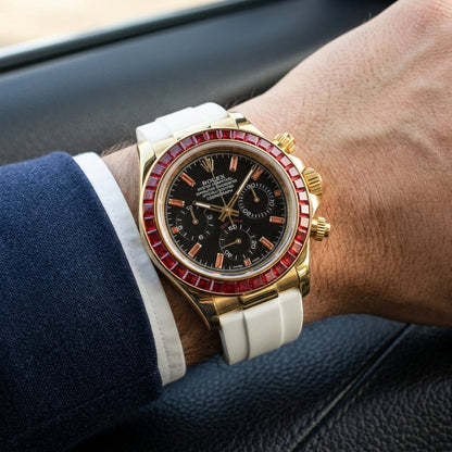 Gold-tone chronograph with a red stone bezel on its white rubber strap, worn on the wrist below a dark suit cuff