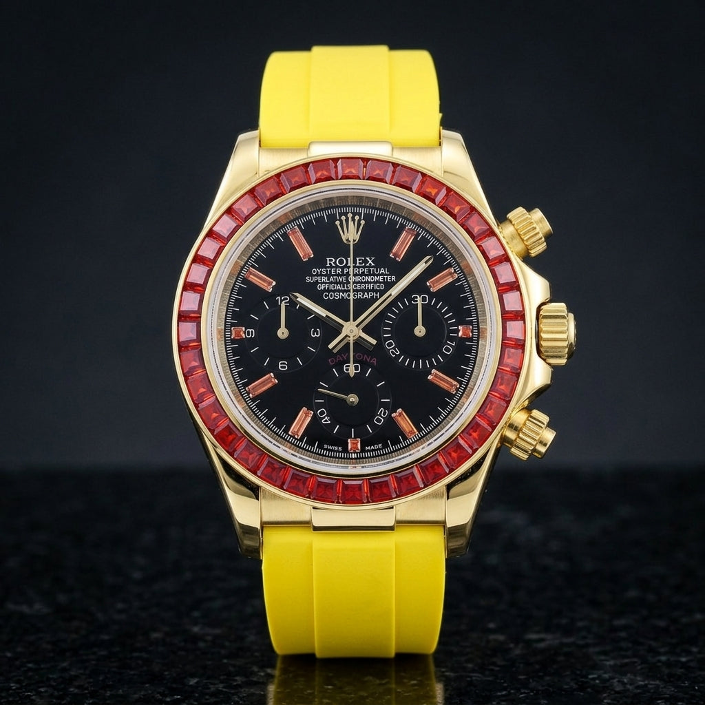 Gold-tone chronograph with a red baguette-stone bezel and a black dial on a bright yellow rubber strap, upright on polished black granite
