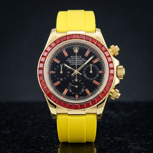 Gold-tone chronograph with a red baguette-stone bezel and a black dial on a bright yellow rubber strap, upright on polished black granite