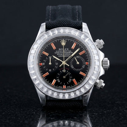 Steel chronograph with a black dial on its black canvas strap, worn on the wrist below a dark suit cuff