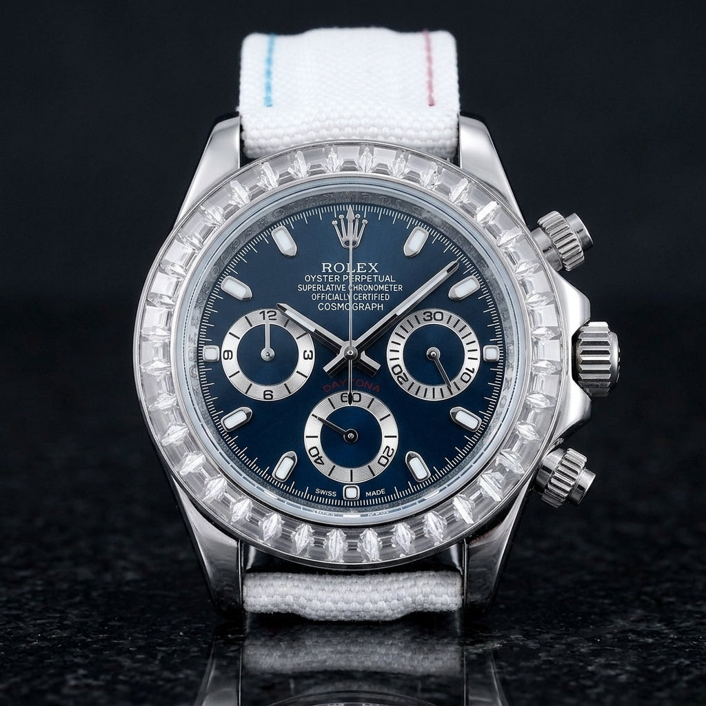 Steel chronograph with a blue dial on its white canvas strap with sky-blue and pink stitching, worn on the wrist below a dark suit cuff