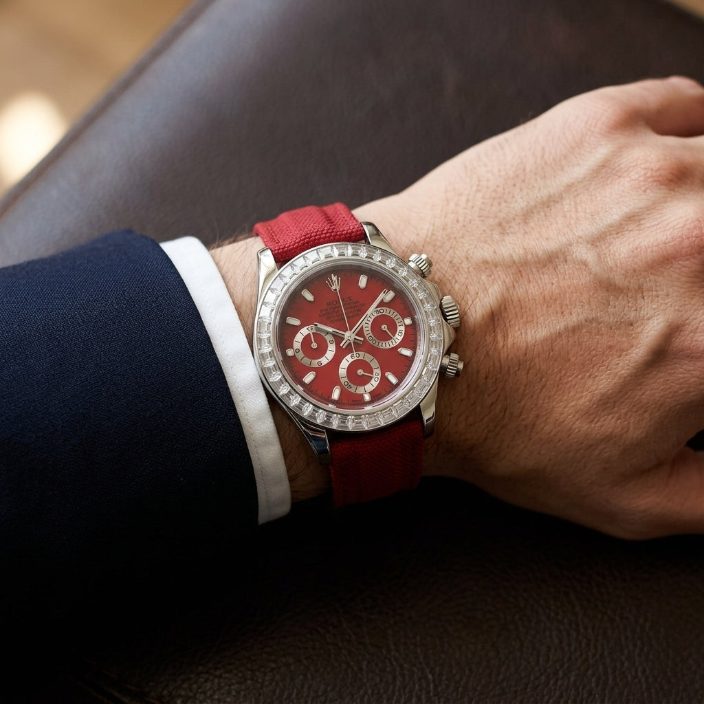 Steel chronograph with a red dial on its red canvas strap, worn on the wrist below a dark suit cuff