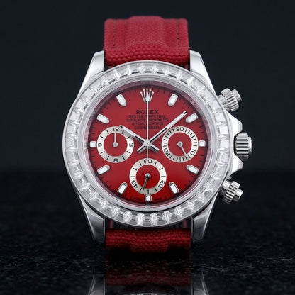 Steel chronograph with a red dial on its red canvas strap, worn on the wrist below a dark suit cuff