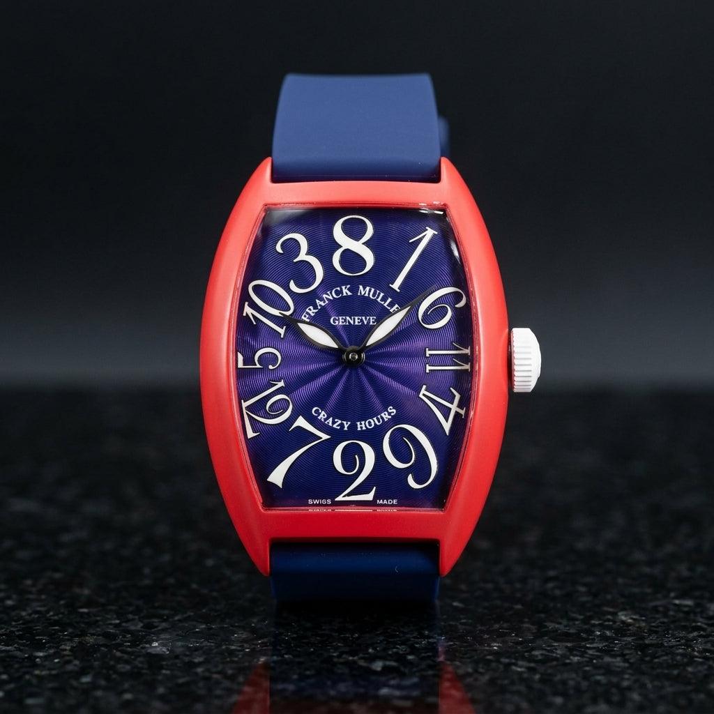 Red curved tonneau watch with a blue dial and white numerals set out of order, upright on polished black granite