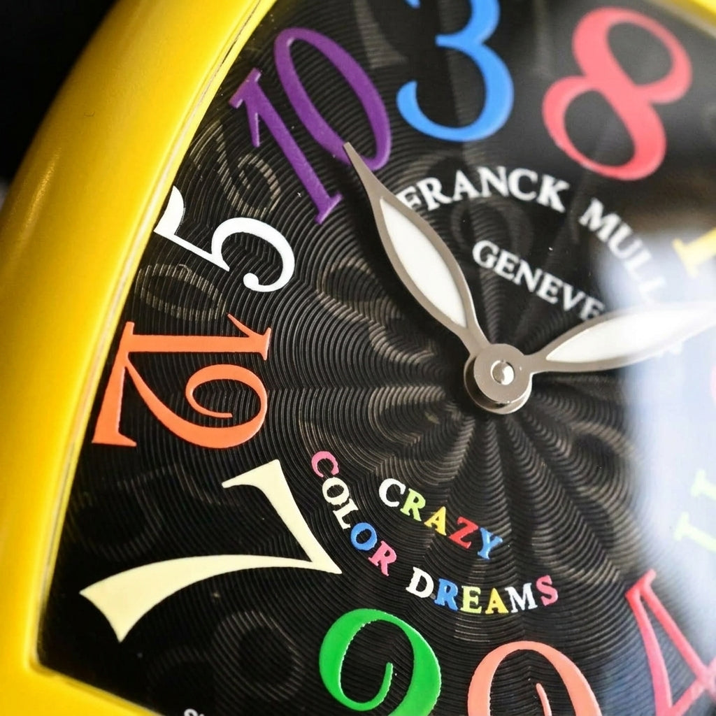 Macro of the black dial with its coloured out-of-order numerals and silver-tone leaf hands inside the yellow case