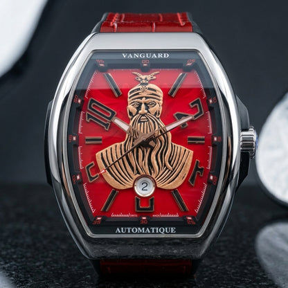 Steel curved tonneau watch with a red dial and a rose-gold-tone bearded warrior bust, upright on polished black granite