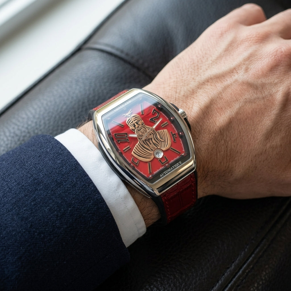 Steel curved tonneau watch with a red dial on its red strap, worn on the wrist below a dark suit cuff