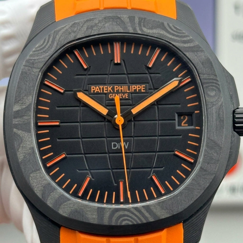 Macro of the matte black globe-grid dial with orange batons, orange minute strokes, orange hands and the date window at three